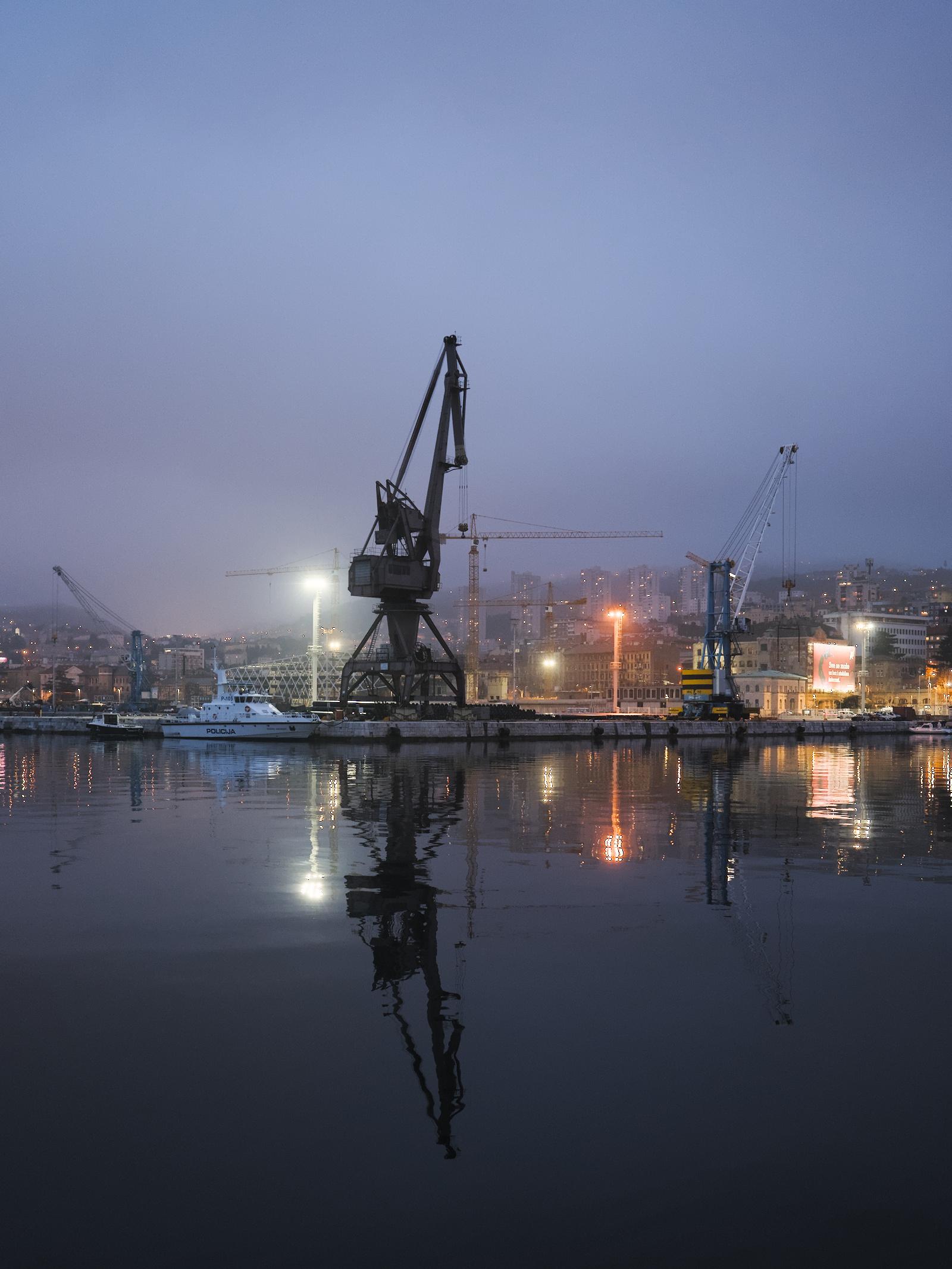 English: A harbour cargo crane at twilight. There is a sombre atmosphere. The crane is reflected in the water.

Deutsch: Ein Lastenkran eines Hafens nach der blauen Stunde. Es herrscht eine düstere Stimmung. Der Kran spiegelt sich im Wasser.
